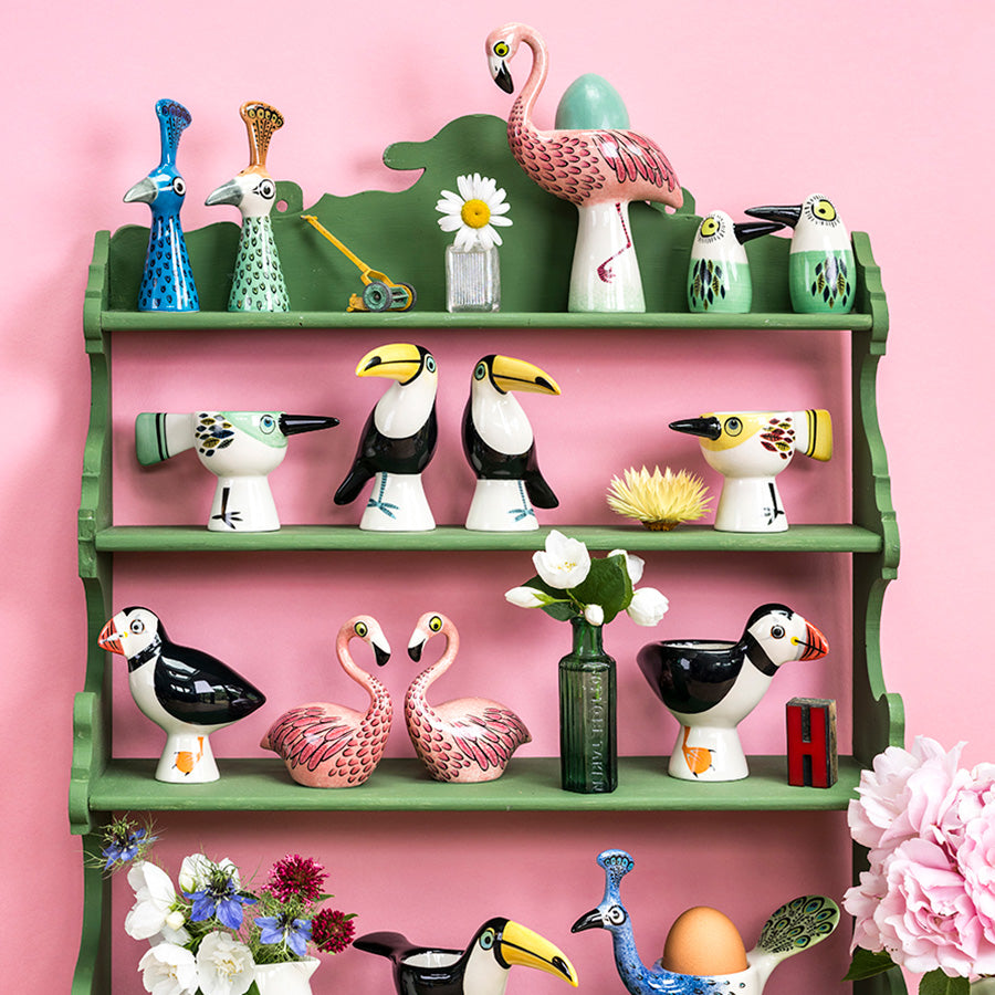 Decorative shelf with colorful bird-themed egg cup and salt 7 pepper shakers  against a pink background