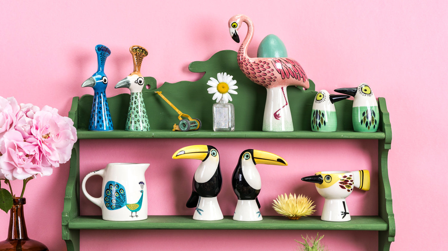 Decorative shelf with colorful bird-themed egg cup and salt 7 pepper shakers  against a pink background