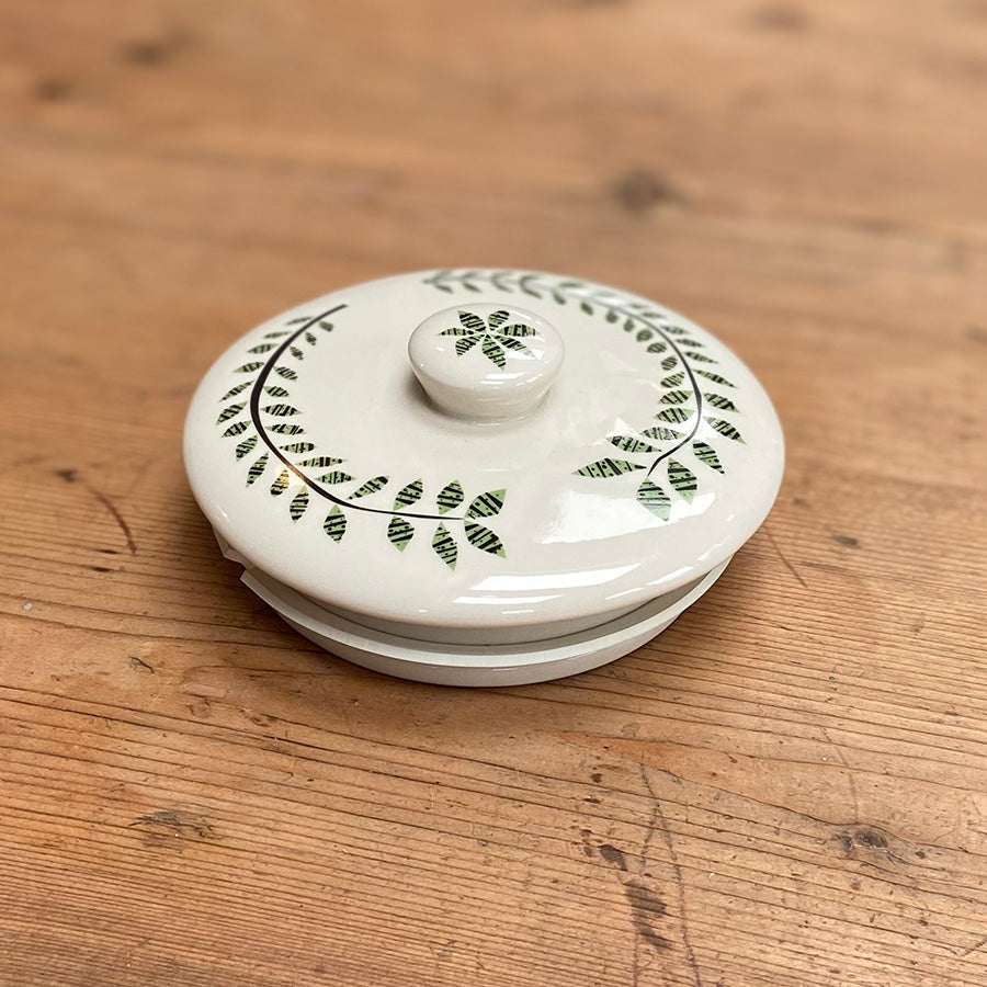 White ceramic lid with decorative green patterns on a wooden surface