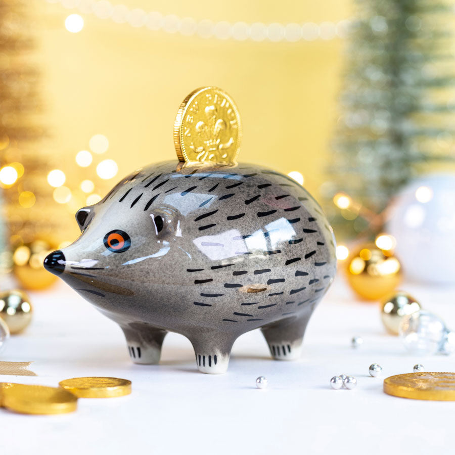 Hedgehog-shaped piggy bank with a gold coin on a blurred festive background