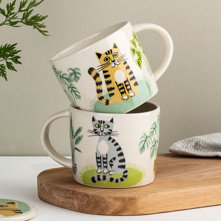 Two mugs with cat illustrations stacked on a wooden surface.