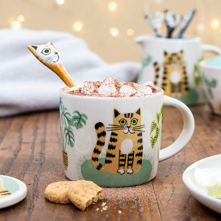 Cat-themed mug with hot chocolate and a cat-shaped spoon on a wooden table.