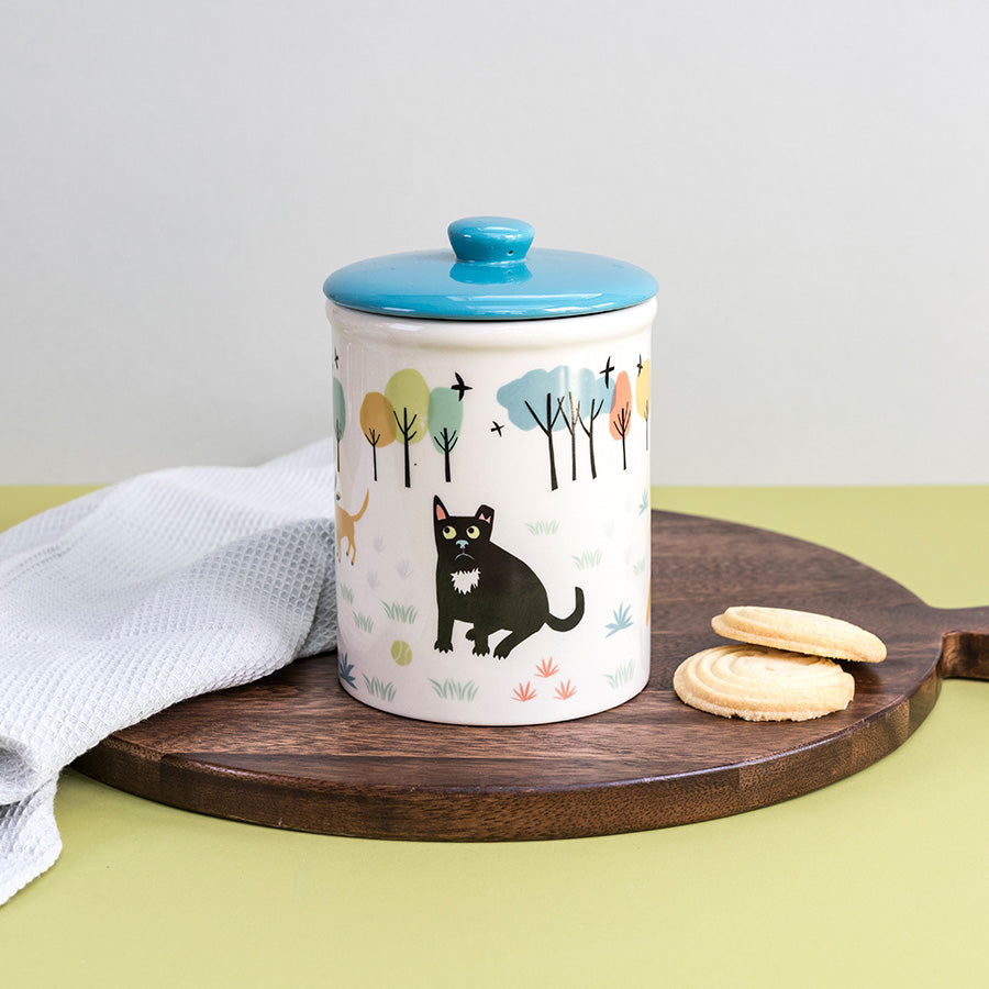 Storage jar with a blue lid on a wooden tray with cookies, against a light gray background.