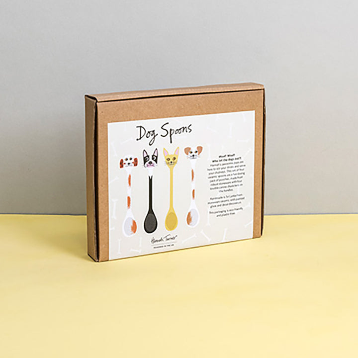 Brown cardboard box of Dog Spoons with illustration on a light grey background with the text 'Hannah Turner designed in the UK'. Packaging shot for Hannah Turner's Ceramic Dog Spoon Set.