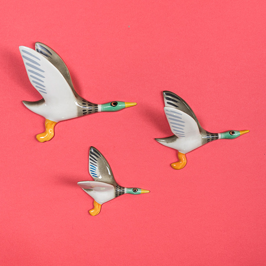 Three flying duck figurines on a pink background
