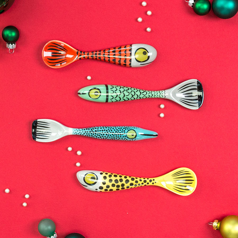Colorful fish-shaped spoons on a red background with Christmas ornaments.