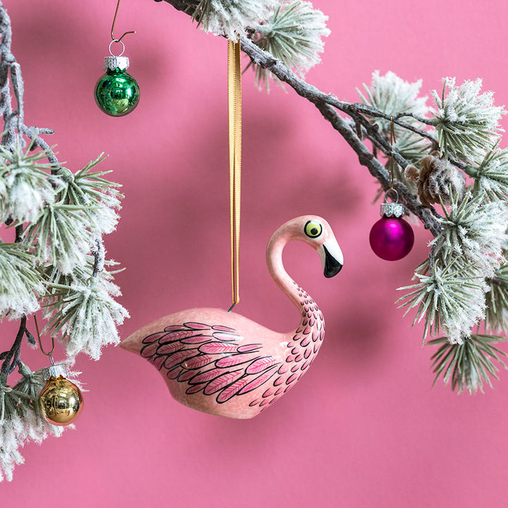 Flamingo ornament hanging on a tree branch with a pink background