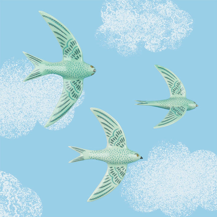Three flying green swifts against a blue sky with white clouds