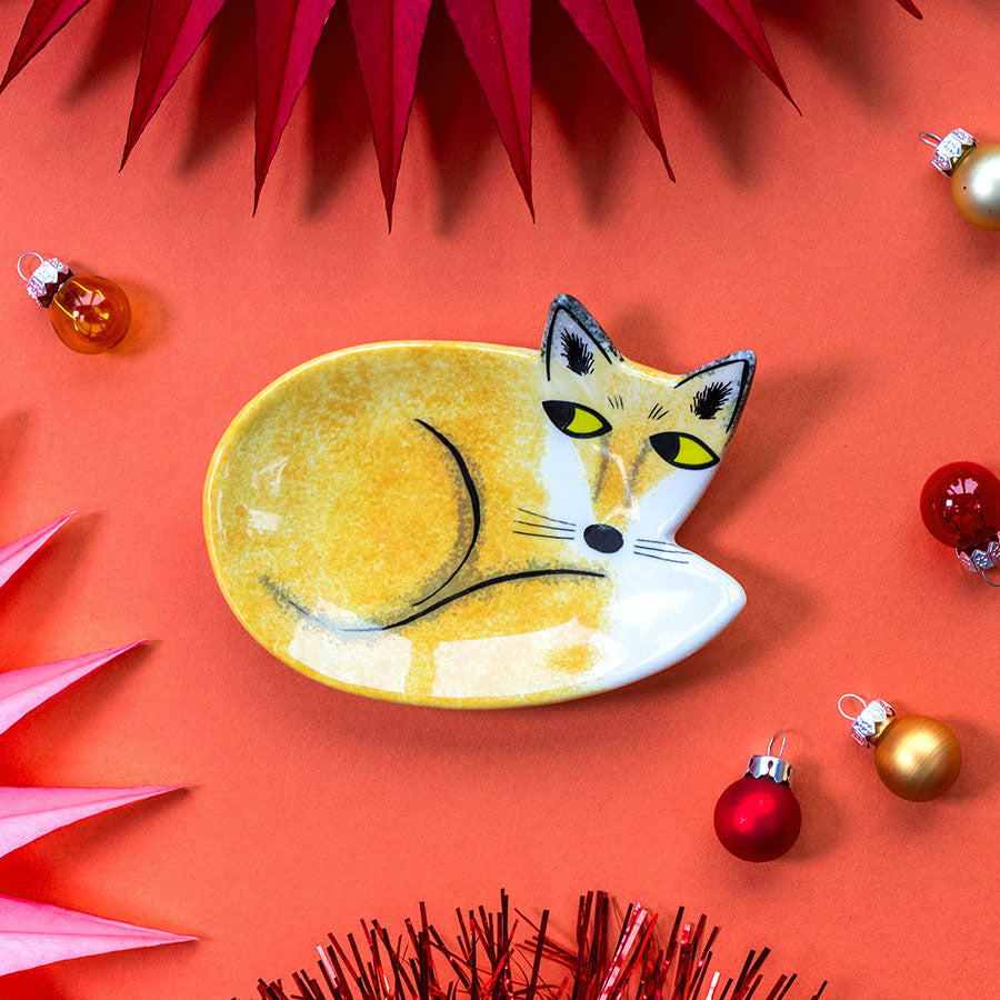 Decorative fox-shaped trinket dish  on a red background with Christmas ornaments.