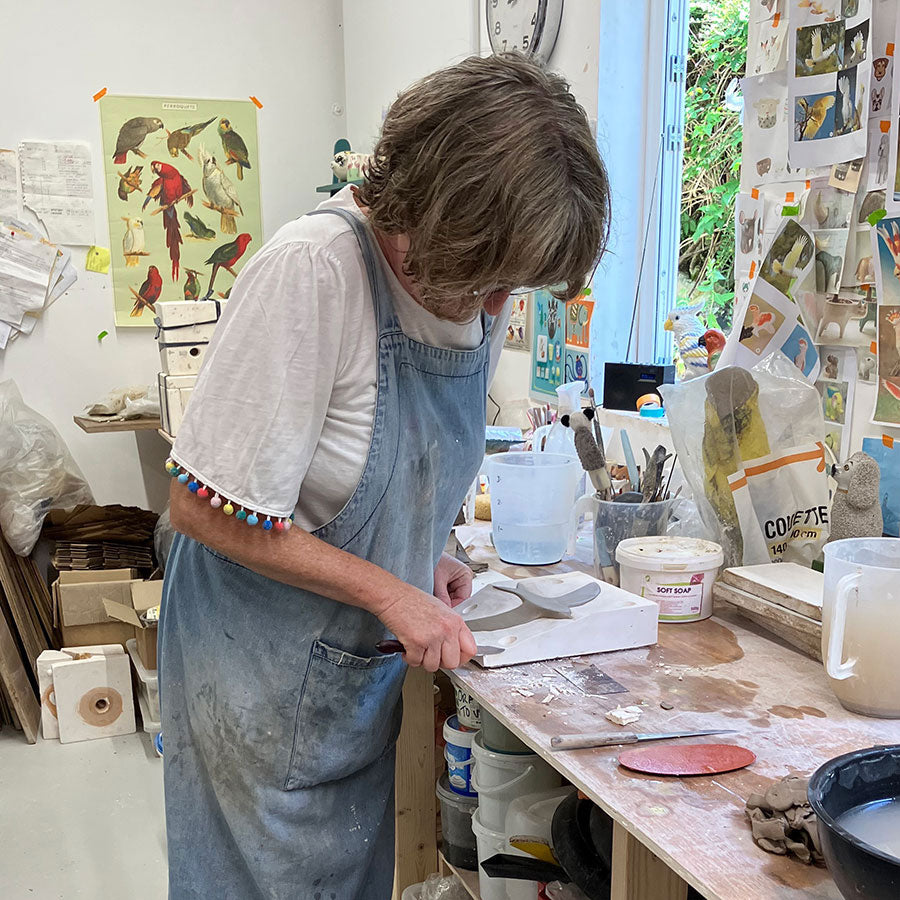 Hannah Turner at a workbench in her pottery studio creating clay swifts with various tools and materials .