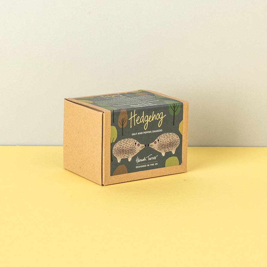 A square kraft paper box for Hedgehog Suet and Pepper Shaker, featuring an illustration of two hedgehogs on a dark green label, set on a yellow surface against a light gray background.