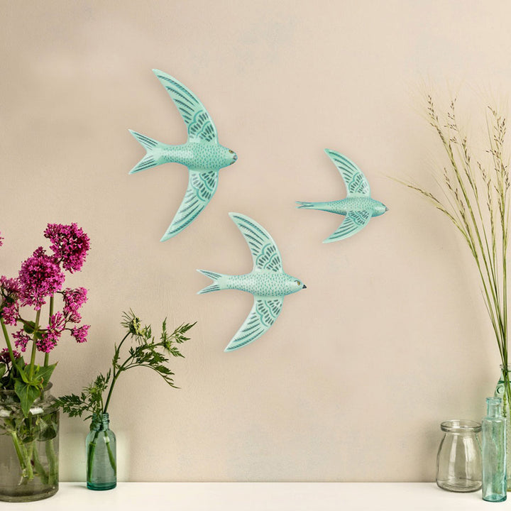 3 Jade Green Flying swifts by Hannah Turner on a plain background, flowers and grasses at the edge. 