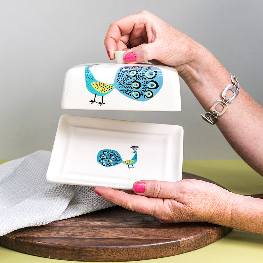 Person holding a ceramic dish with peacock design on a wooden surface