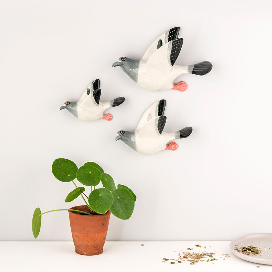 Three ceramic pigeon figurines on a white surface with a potted plant and small plate.