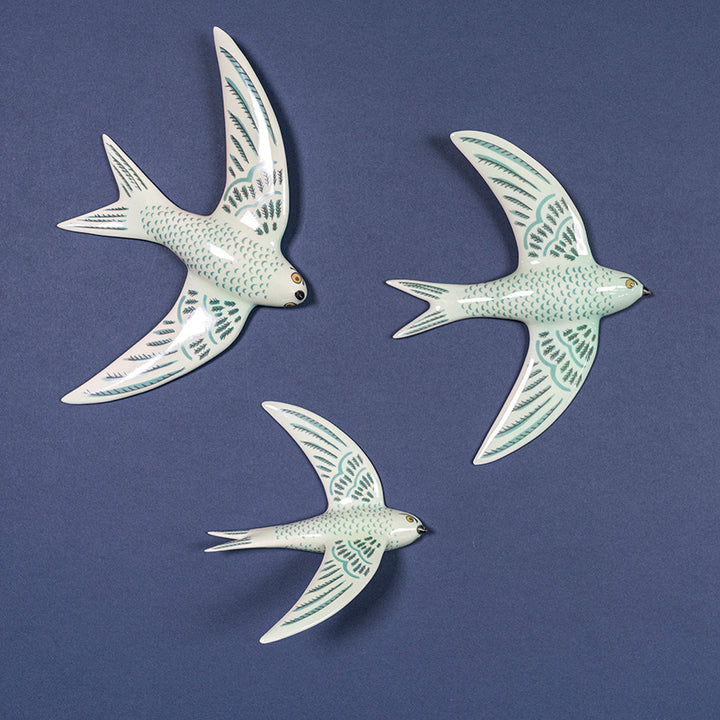 Three ceramic jade green swifts wall art pieces on a blue background