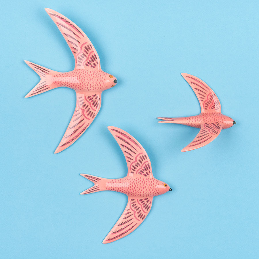 Three pink ceramic flying swifts wall art by Hannah Turner on a blue background.