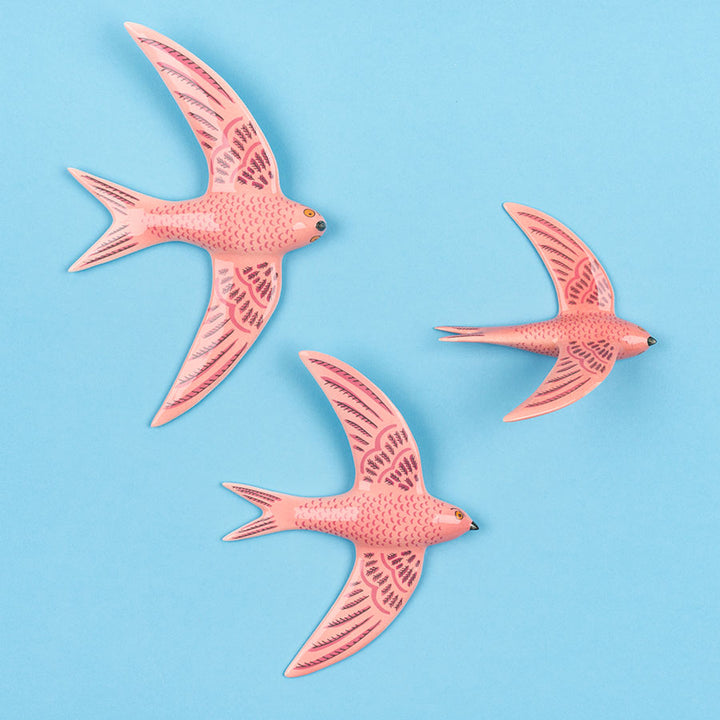 Three pink ceramic flying swifts wall art by Hannah Turner on a blue background.