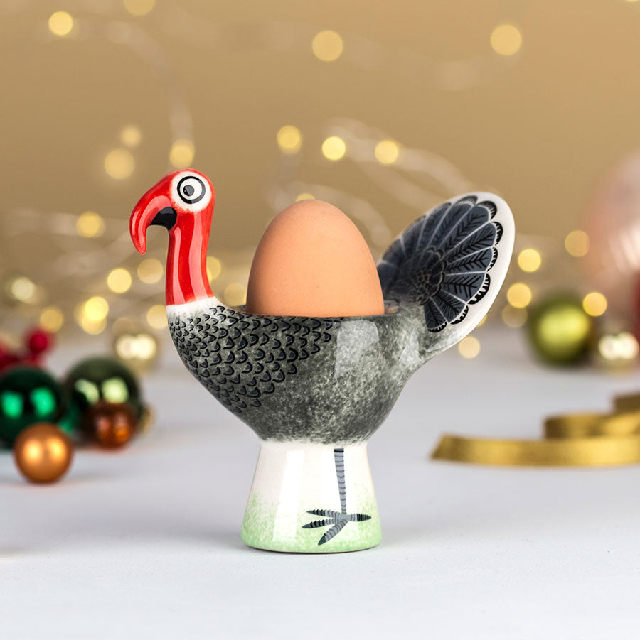 Decorative egg cup shaped like a turkey with a brown egg on a blurred festive background.