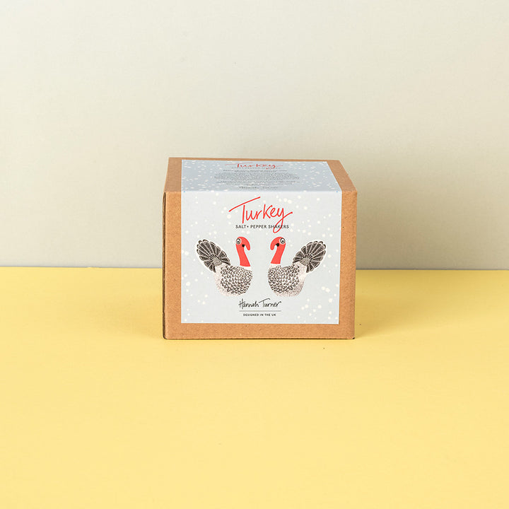 A square kraft paper box with a white front label featuring two illustrated turkeys and the text 'Turkey' and Salt & Pepper Shakers standing on a yellow surface against a light beige wall.