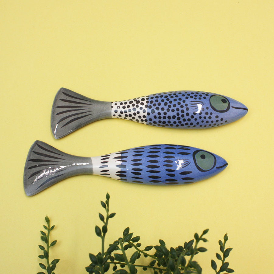 Two fish wall ornaments on a yellow background with green leaves at the bottom.